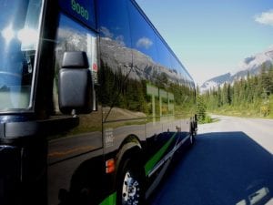 black tcs canada charter bus in alberta on mountain road with mountain reflected on the bus