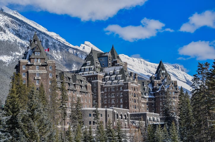 Historic Banff Springs Hotel in Banff National Park set in front of snow capped mountains and large pine trees