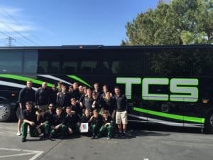 sports team standing in front of black tcs branded charter bus